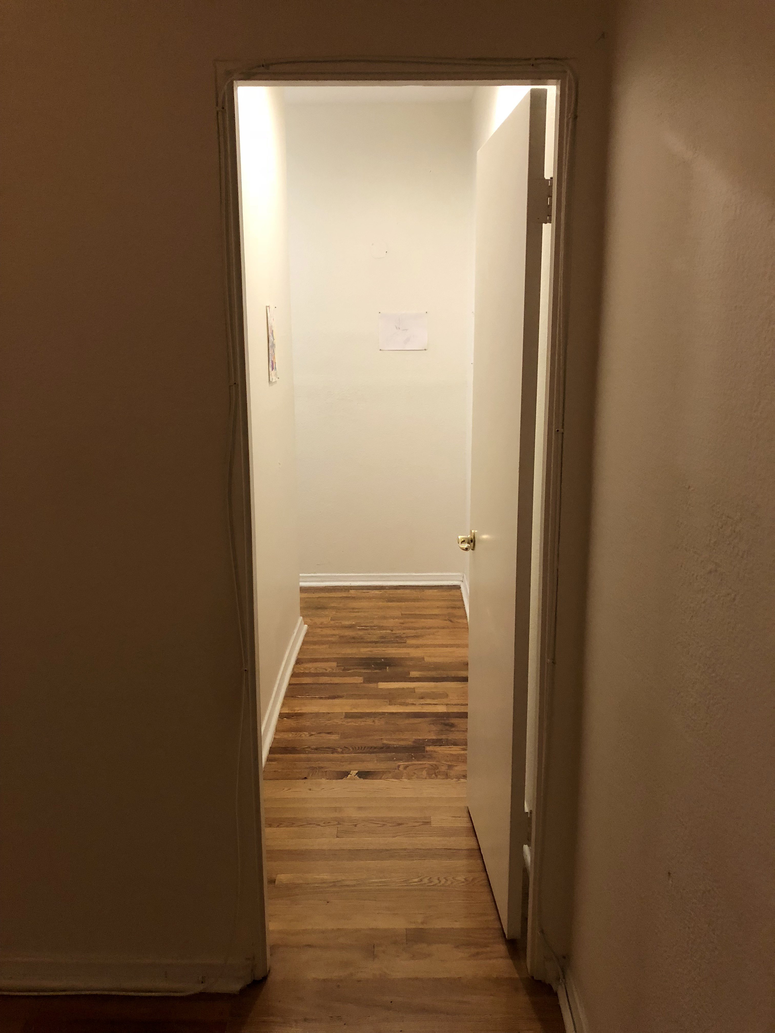 A narrow white hallway seen from an open door